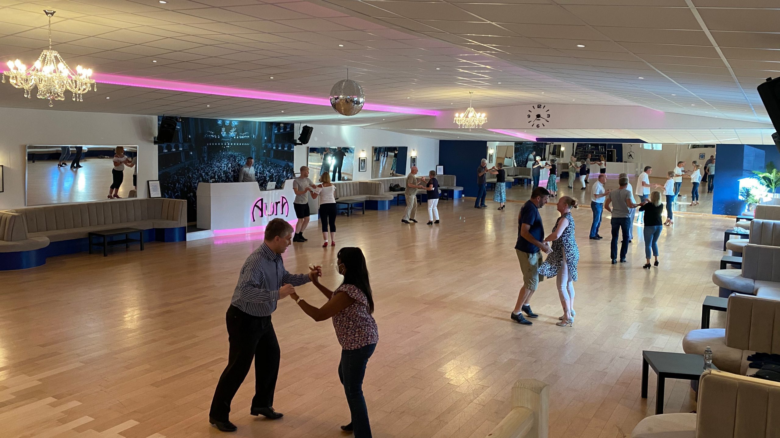Adult couples practicing partner dancing across the ballroom at AURA Dance Studios